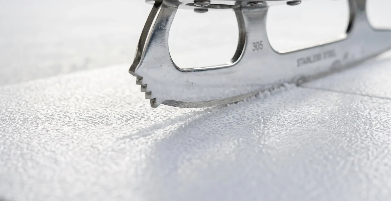 Gros plan d'une lame de patin professionnel en métal chromé en contact avec la surface texturée d'une dalle de patinoire synthétique PEHD blanche