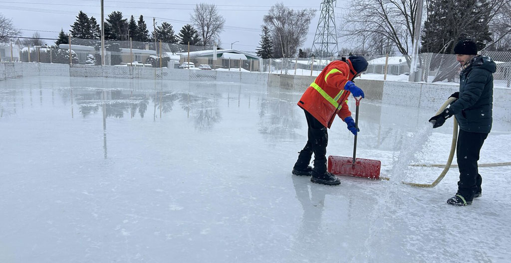 Technicien événementiel en tenue professionnelle effectuant l'affûtage d'une lame de patin avec une affûteuse portative dans la zone de chaussage, participants en arrière-plan
